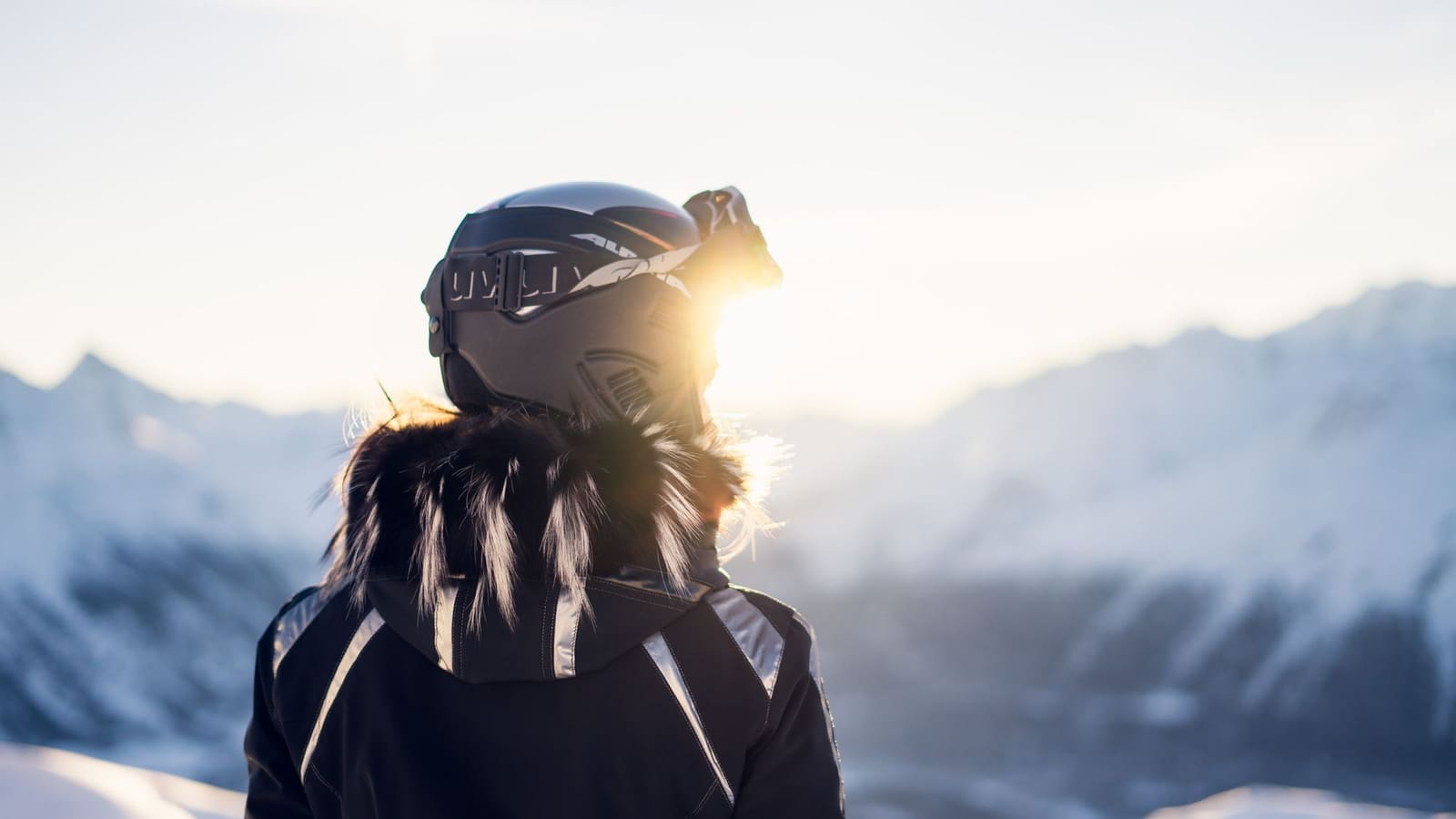 Person i skihjelm og skibriller foran fjell i motlys